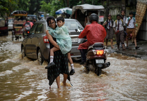 Waterlogging in India Guwahati, India. 25 May 2022. A woman returns her son from school wades across a flooded street after heavy rains, in Guwahati. Waterlogging is a common scene in Guwahati city due to poor drainage system. assam india stock pictures, royalty-free photos & images