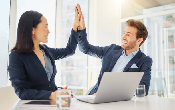 istock Two happy young diverse colleagues giving each other a high five while working together on a laptop in an office. Excited caucasian businessman celebrating a winning success with motivated asian businesswoman 1399215188
