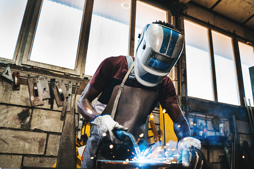 A skilled welder is seen at work in a large industrial factory, using a welding machine to repair a metal plate