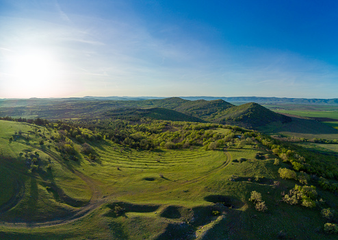 Bird's eye view panorama of spring blooming green meadows and wooded hilly slopes of the Balkan Mountains, under the light of a bright cloudy warm day in the country of Bulgaria
