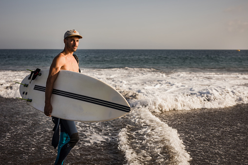A well-built young man carries a surfboard, ready to spend the day on the sea waves.