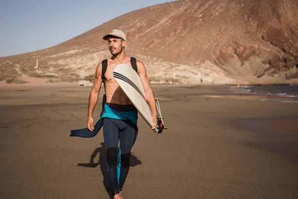 A well-built young man carries a surfboard, ready to spend the day on the sea waves.