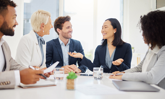 Diverse group of people meeting and working at a board room table at a business presentation or seminar. The documents on the conference table have financial or marketing figures, graphs and charts on them.