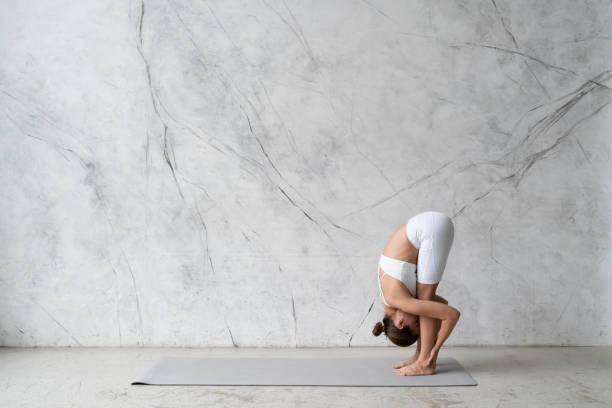 istock Young woman in white outfit practicing yoga standing forward bend, uttanasana 1399218192