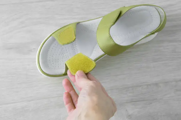Green women's leather sandals on a white wooden background. He stretches the Velcro fastener with his hand.