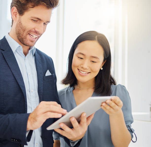 istock Two happy young diverse colleagues working together on a digital tablet in an office. Confident asian businesswoman and smiling caucasian businessman discussing corporate plans and ideas while using apps on device 1399225236