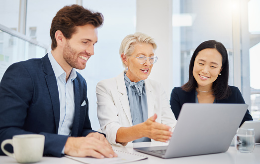 Group of happy diverse businesspeople discussing corporate plans together while brainstorming on a laptop in an office. Mature caucasian female boss explaining ideas and strategies to her young smiling colleagues
