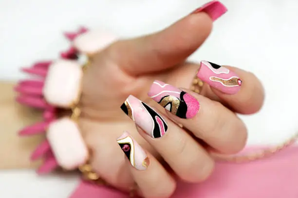 Abstract manicure with multicolored lines on pink nail polish.