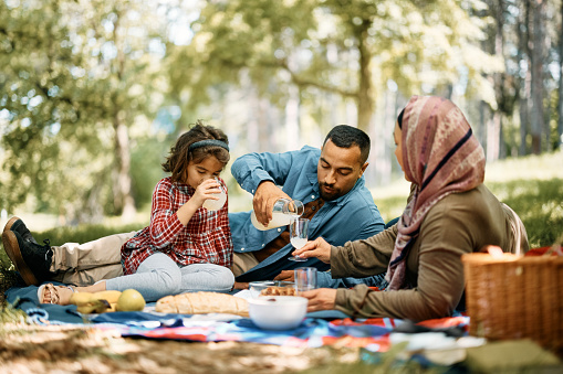 Muslim parents and their small daughter drinking lemonade while enjoying on picnic in springtime.