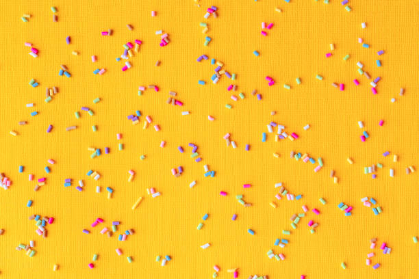 Colorful sprinkles on yellow background. Concept of fun and celebration. Spring, summer mood. Confectionery decorating ingredients on paper making pattern. Backdrop for party invitation card design