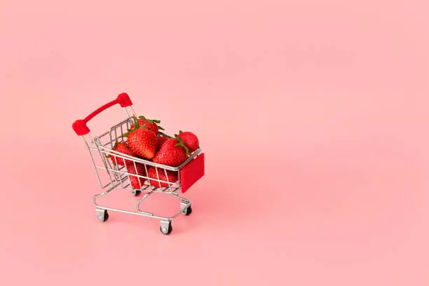 Fresh red strawberry in shopping card on pink background. Online shopping and Valentines Day minimalistic concept. Black Fridays sales banner. Healthy, organic, vegan food