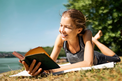 Happy young woman reading a book in public park