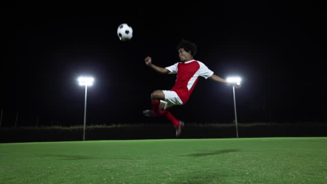 Powerful soccer player kicking the ball in the air at the field while playing a game at nighttime