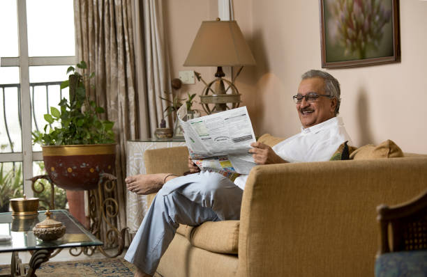 Senior man reading newspaper while sitting on sofa in the living room