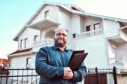 Balding Male Real Estate Agent Carrying Clipboard For House Demonstration