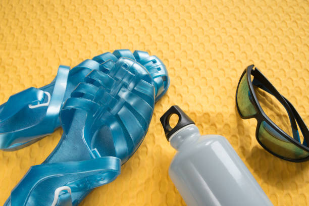 Vacation concept. Sunglasses, water bottle and plastic sandals for the beach. Yellow background