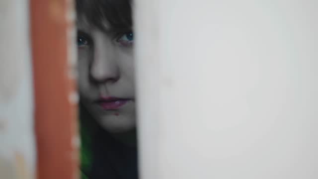 The boy looks out fearfully through the crack between the doors. He looks warily at the camera. Close-up