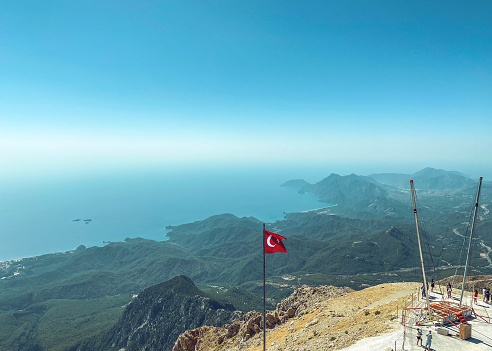 mountains in a hot, tropical country against a blue sky. green plants grow on the mountains. the Turkish flag is set on the observation deck on the top of the mountains.