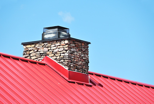 Stone chimney on red metal roof.