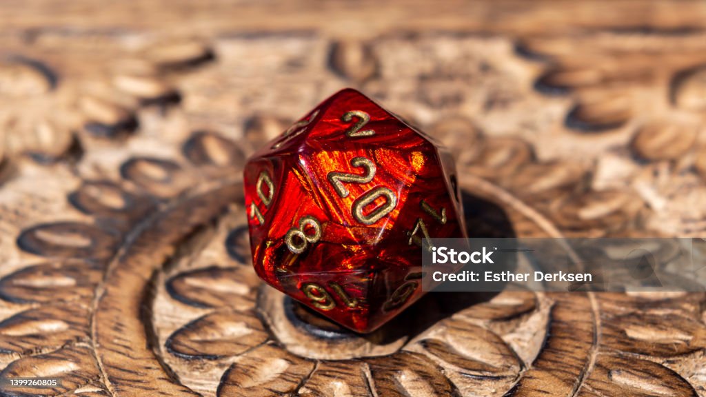 Close-up image of a red d20 on a wooden surface Close-up image of a red 20-sided role-playing gaming die on a wooden surface Dragon Stock Photo