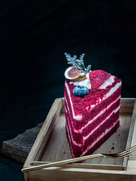 Piece of red velvet cake served with small brass fork on wooden tray. Selective focus.