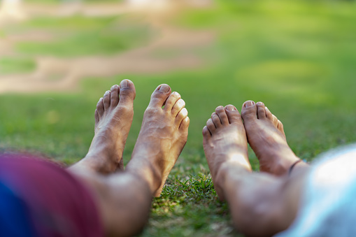 Selective focus on the feet of two relaxed and barefoot latin men in the grass of a park