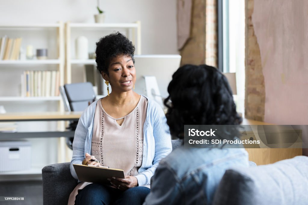 Mature female counselor gives unrecognizable young woman advice As they meet in her office, the mature adult female therapist gives the unrecognizable young adult woman advice. Mental Health Professional Stock Photo