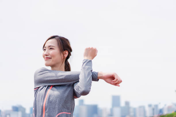giovane donna che si allunga all'aperto con un sorriso - running jogging asian ethnicity women foto e immagini stock