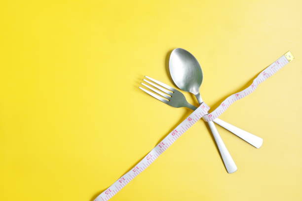 Fork and spoon wrapped with measuring tape flat lay in yellow background. Anorexia, Diet and nutrition to lose weight concept.