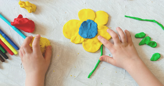 Hands of little girl making flower and sun and other  from colorful clay dough, plasticine, Home Education game with clay. Early development concept. Educational and entertaining classes with children