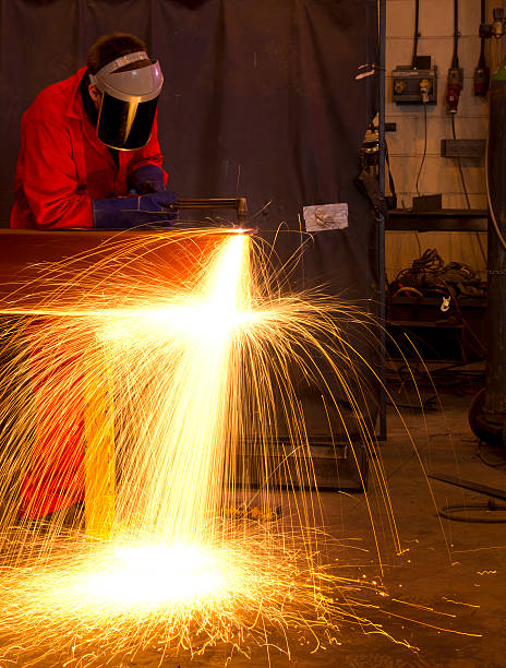 istock Welder bends to cut metal beam with orange sparks. 139929724