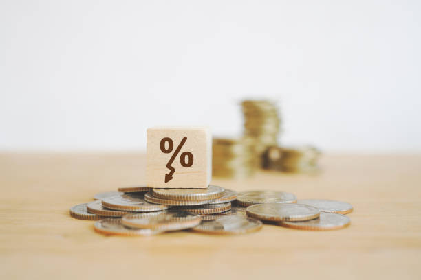 decreasing percent sign on wooden cube block on pile of coins and blurred stack of coins stock photo