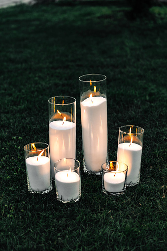 Lighted decorative candles. On the grass are candles burning glass cylinders