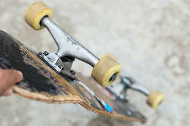 man holds used skateboard in his left hand on a concrete background