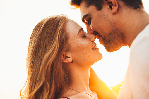 Close-up portrait of a woman and man closing their eyes and wanting to kiss with the sun shining behind them. Side view. Close-up portrait.