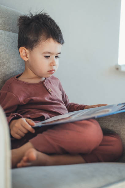 istock School-age boy reading a book while siting comfortable on the couch doing his homework to school. Distance education. Close up. 1399310898