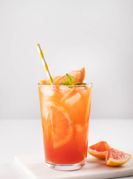 istock Fresh grapefruit juice with ice, mint and grapefruit slice in a glass on a white marble background with citrus  slices close up. Front view 1399311856