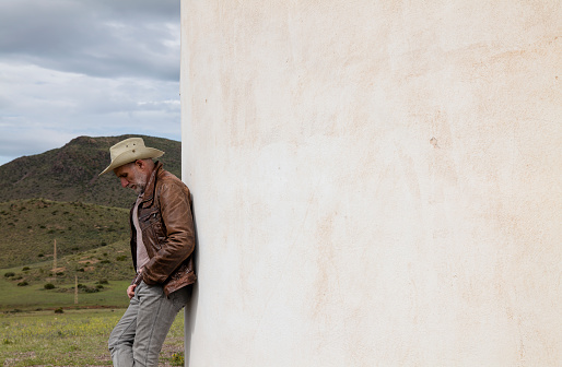 Adult man in cowboy hat standing against white wall in field