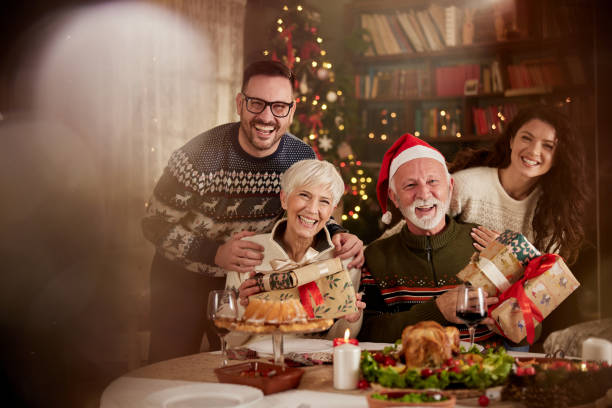 Happy senior parents and their adult children on Christmas day in dining room. Happy adult children and their senior parents enjoying in dining room on Christmas day and looking at camera. father in law stock pictures, royalty-free photos & images