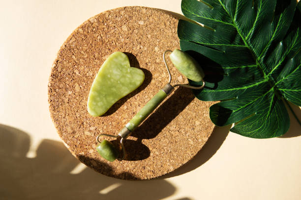 istock Jade Gua sha scraper and face roller massager on a cork round stand with a monstera leaf. 1399317913