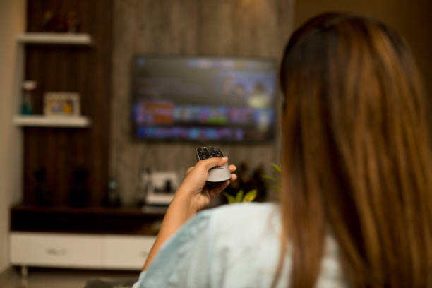 Woman watching tv using remote control stock photo
