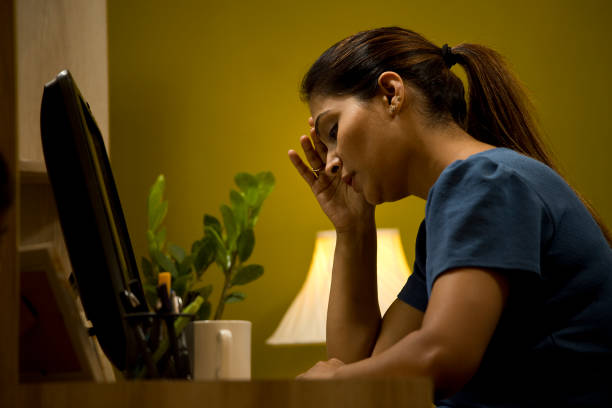 Profile of tired young woman working late night on desktop pc at home