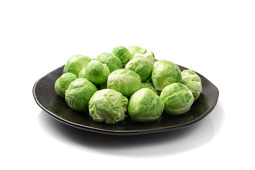 Brussels sprouts isolated. Brassica oleracea cabbage on black plate, raw edible buds on white background top view
