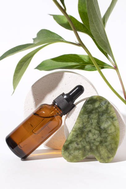 istock Cosmetic bottle with dropper on podium, jade Gua sha stone for face massage. Serum container and plant twigs on white background. Organic cosmetics, beauty products concept. 1399331724