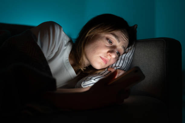 woman using mobile phone while lying in bed at night, suffering from post-breakup insomnia. anxiety. - waiting telephone on the phone anxiety imagens e fotografias de stock