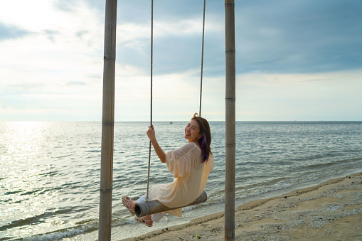Beautiful Asian woman enjoying sea view on swing by the sea in summer time.