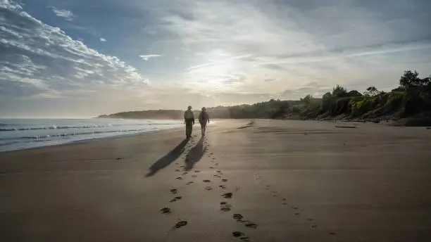 Couple walking on the beach. Sun shining through the clouds, New Plymouth.
