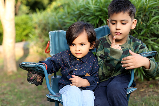 Siblings sitting portrait together on the chair outdoor in nature during summer season.