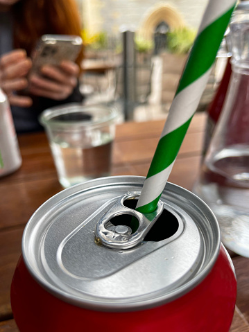 Stock photo showing close-up view of restaurant table setting with can of carbonated drink with green and white striped drinking straw placed through ring pull.