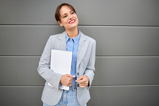 Portrait of successful Caucasian woman businesswoman dressed in stylish suit holding in hand folder  while standing outdoors